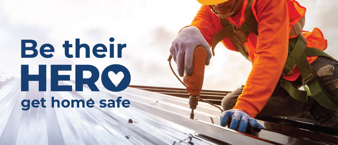 Roof worker wearing fall protection equipment on metal roof next to Be their Hero logo